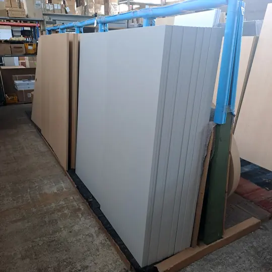 Blick in ein Lager mit vielen an einer Wand aufgestellten Tischplatten in verschiedenen Dekoren 