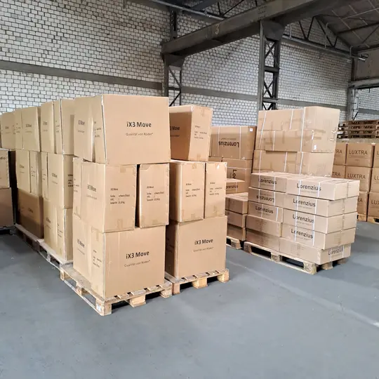 Blick in ein Lager mit vielen Kartons auf Paletten in denen Bürostühle verpackt sind 