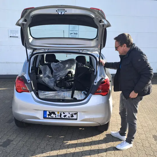 Kunde mit einem neuem Bürodrehstuhl vor seinem Auto Einladen in den Kofferraum 